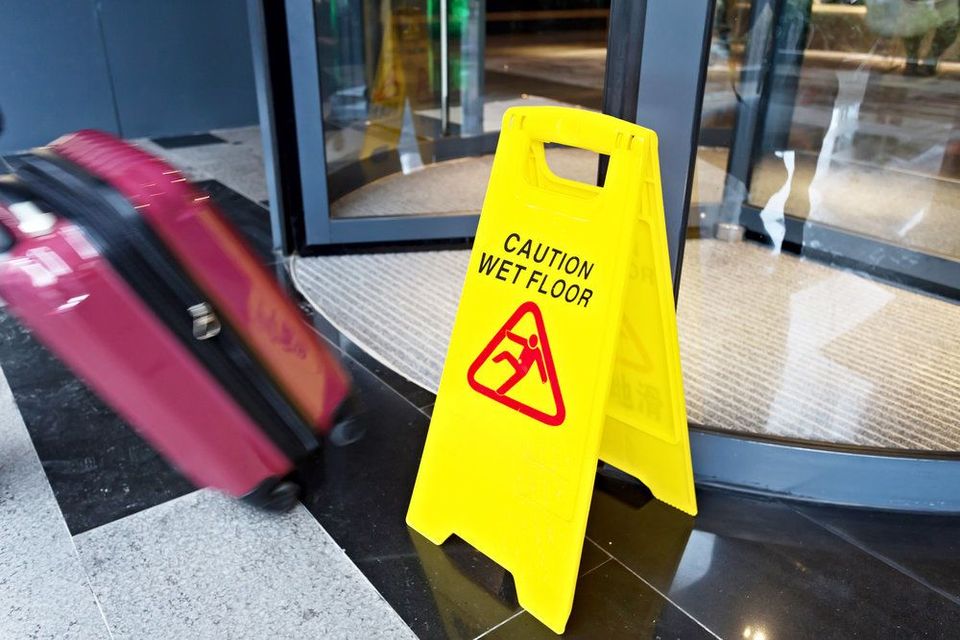 Caution slippery surface sign next to revolving door and rolling suitcase