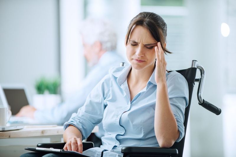 woman in wheelchair, rubbing her temple